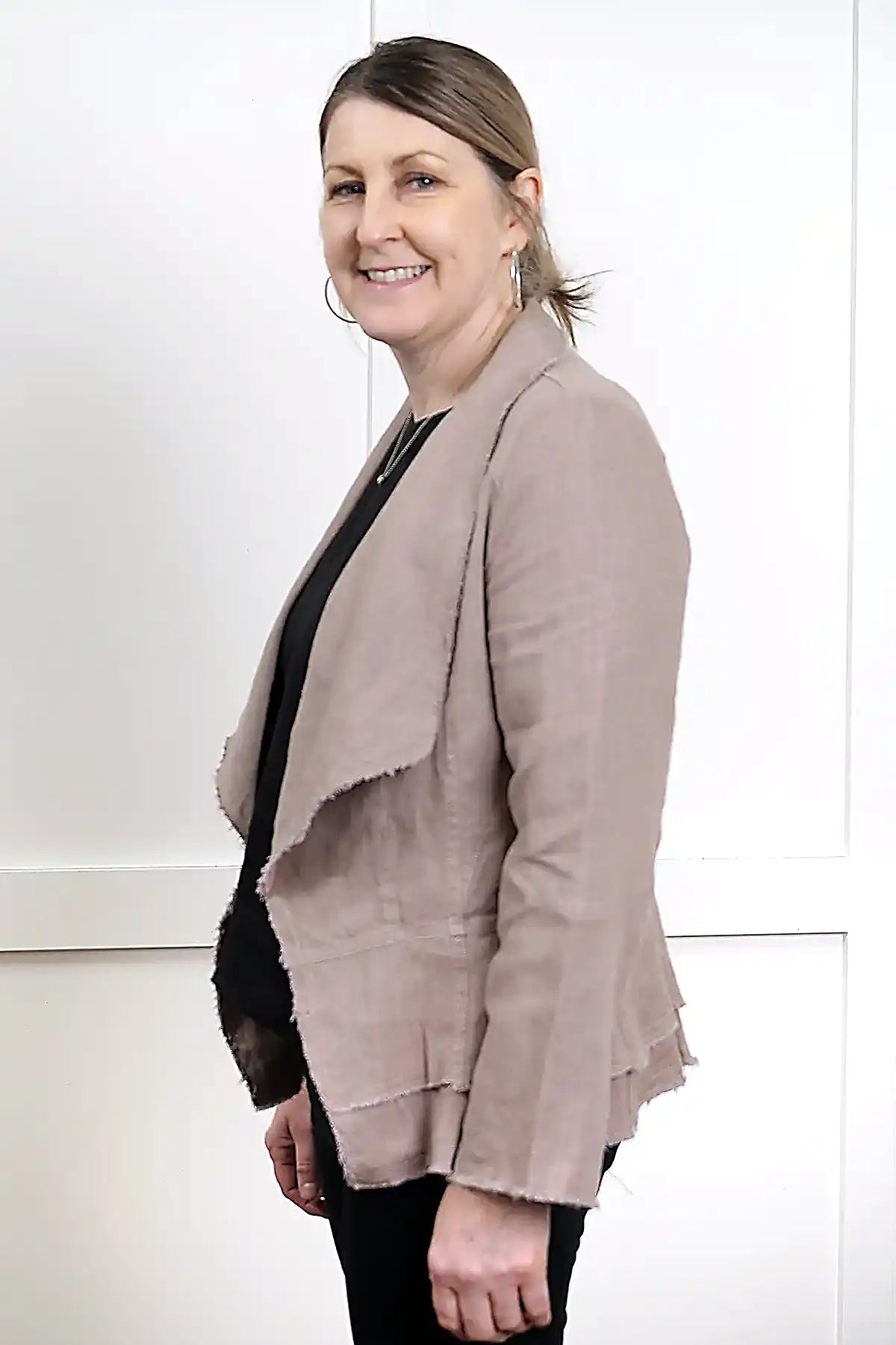 woman wearing a Francesca Linen Jacket in Mushroom with black tee and jeans against a white wall standing side on
