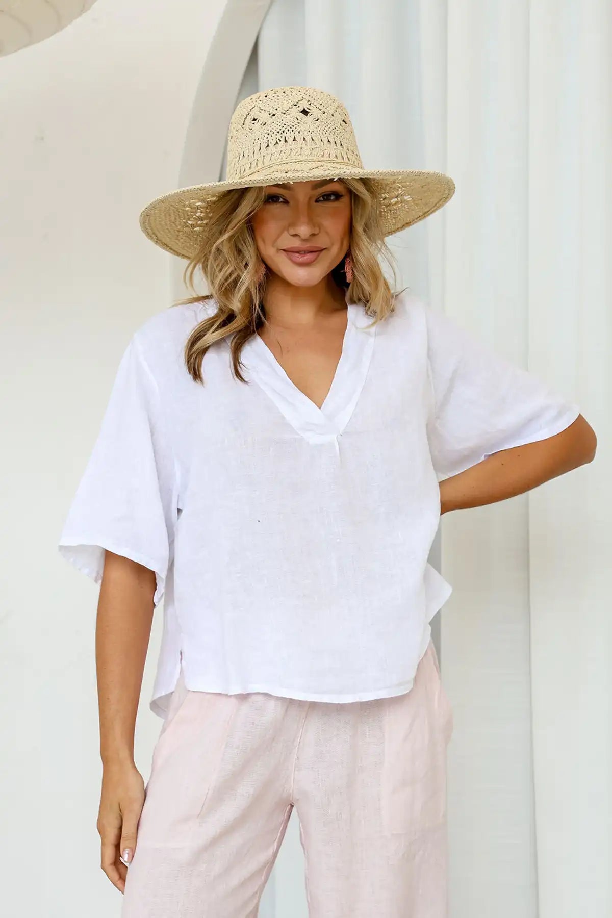 Woman wearing a Gemma Italian Linen White Top and light-colored pants with a straw hat against a neutral background