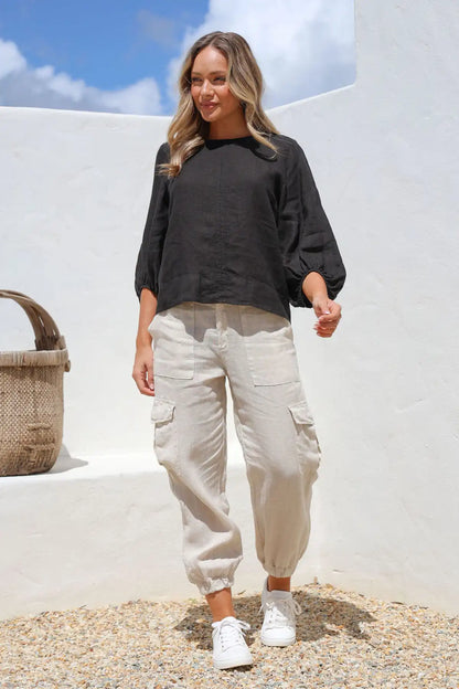 Woman wearing a Giovanna Italian Linen Top in black and beige cargo pants standing against a white wall with blue sky front view.