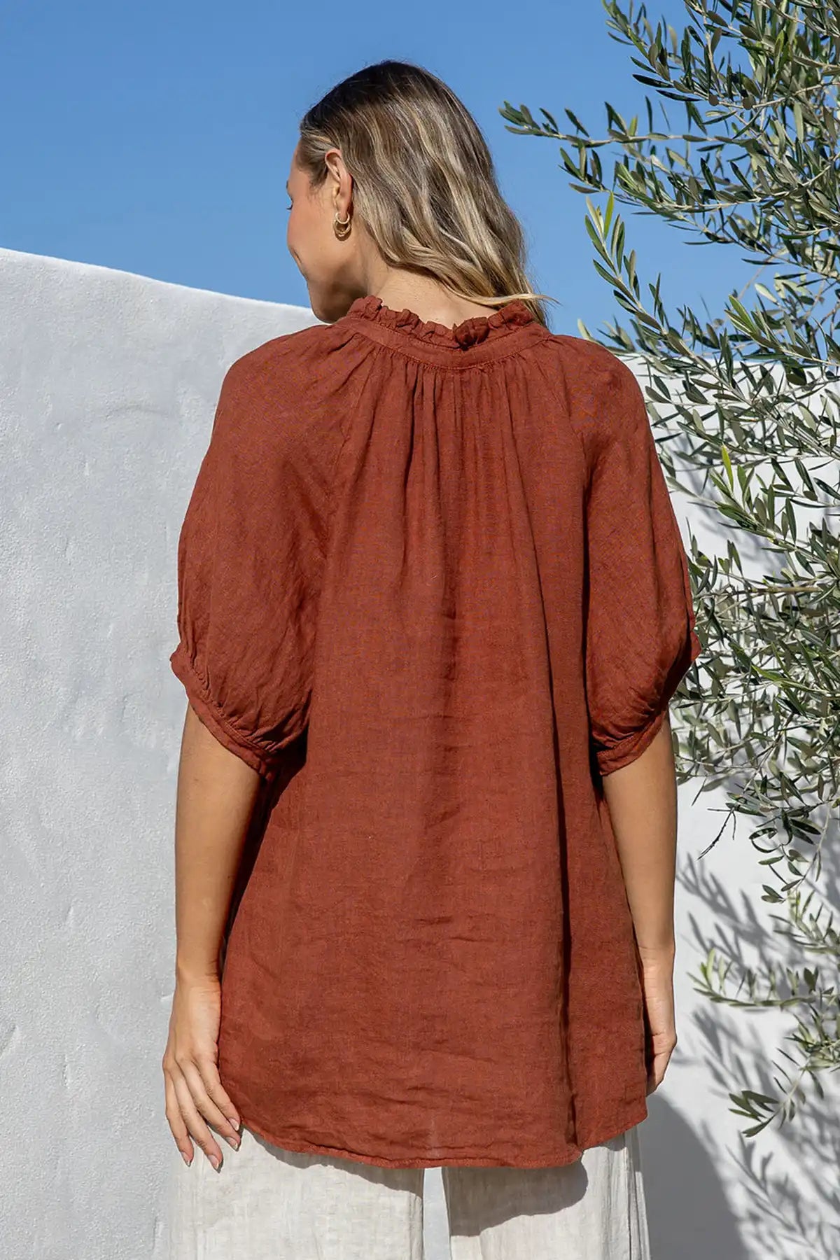 Woman wearing a Giulia Italian Linen Coco Top standing with her back to camera against a white wall with greenery.