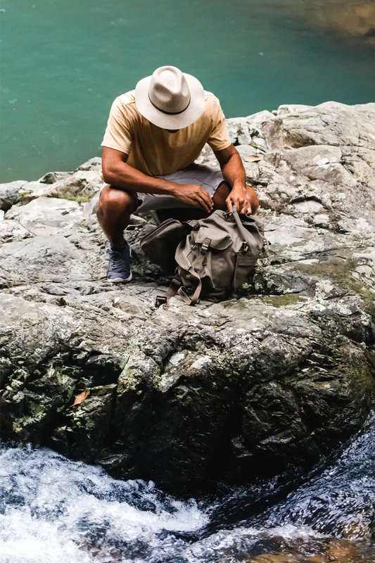 Man sitting on a rock wearing a Rajah felt hat surrounded by water
