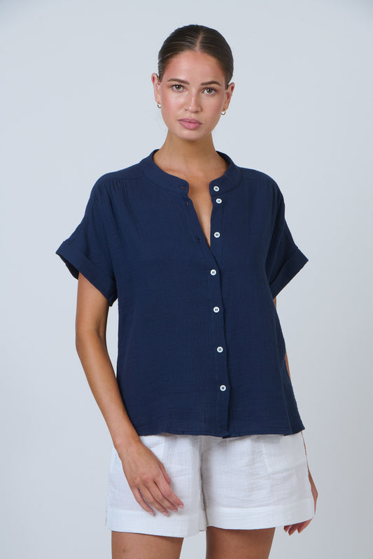 Woman wearing a navy blue button-up shirt and white shorts on a plain background