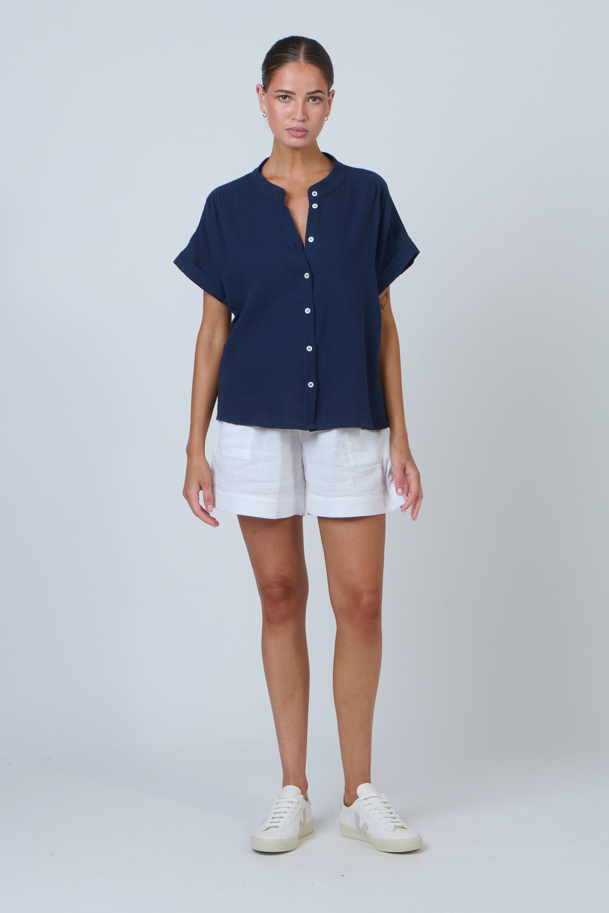 Woman wearing a navy blue shirt and white shorts on a plain background