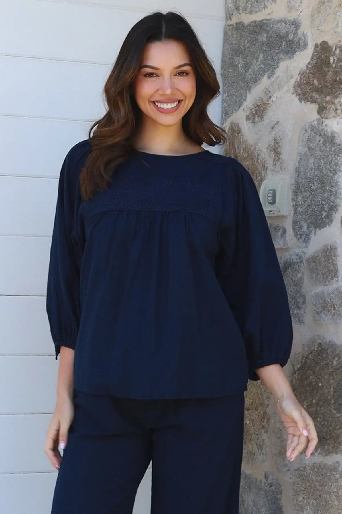 Woman wearing a navy blue outfit standing against a stone wall.