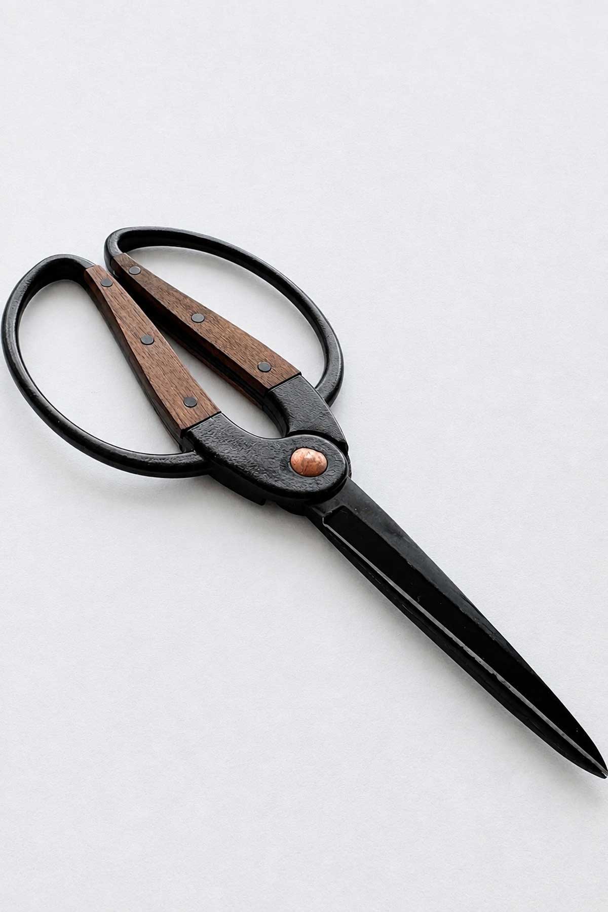 A pair of pruning scissors with black metal blades and handles, featuring brown wooden inlays and a copper-colored center rivet, shown on a light gray background.