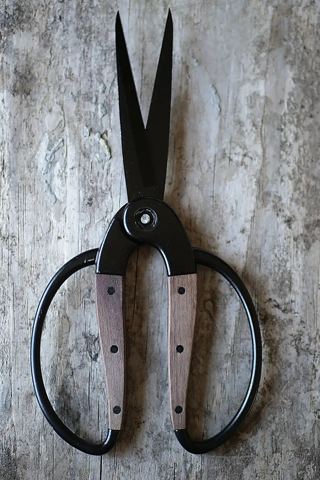 Large black metal shears with wooden handles, laid flat on a weathered gray wood surface.