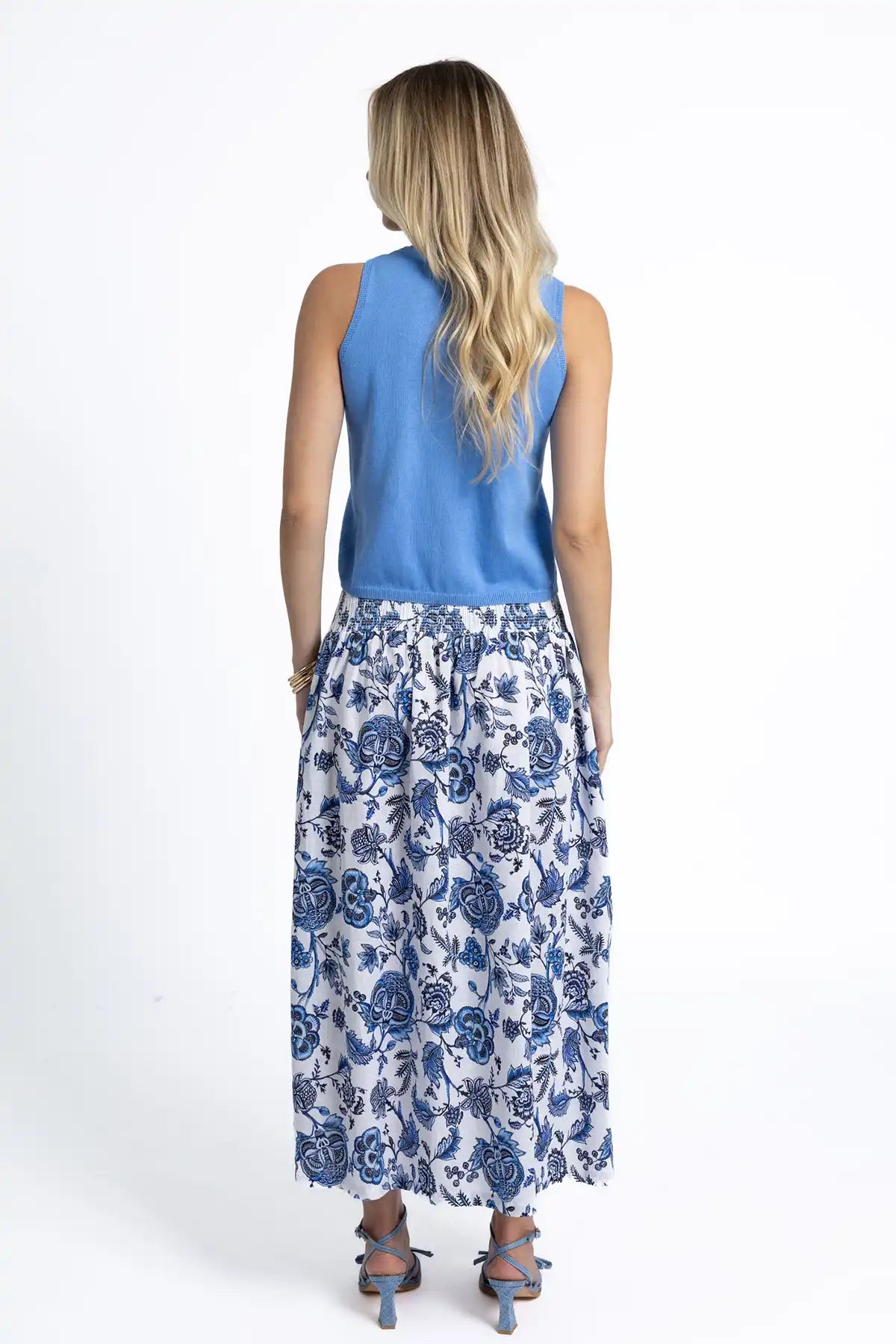 Woman wearing a Humidity Collette Tank in Cornflower Blue and floral skirt with back to camera on a white background