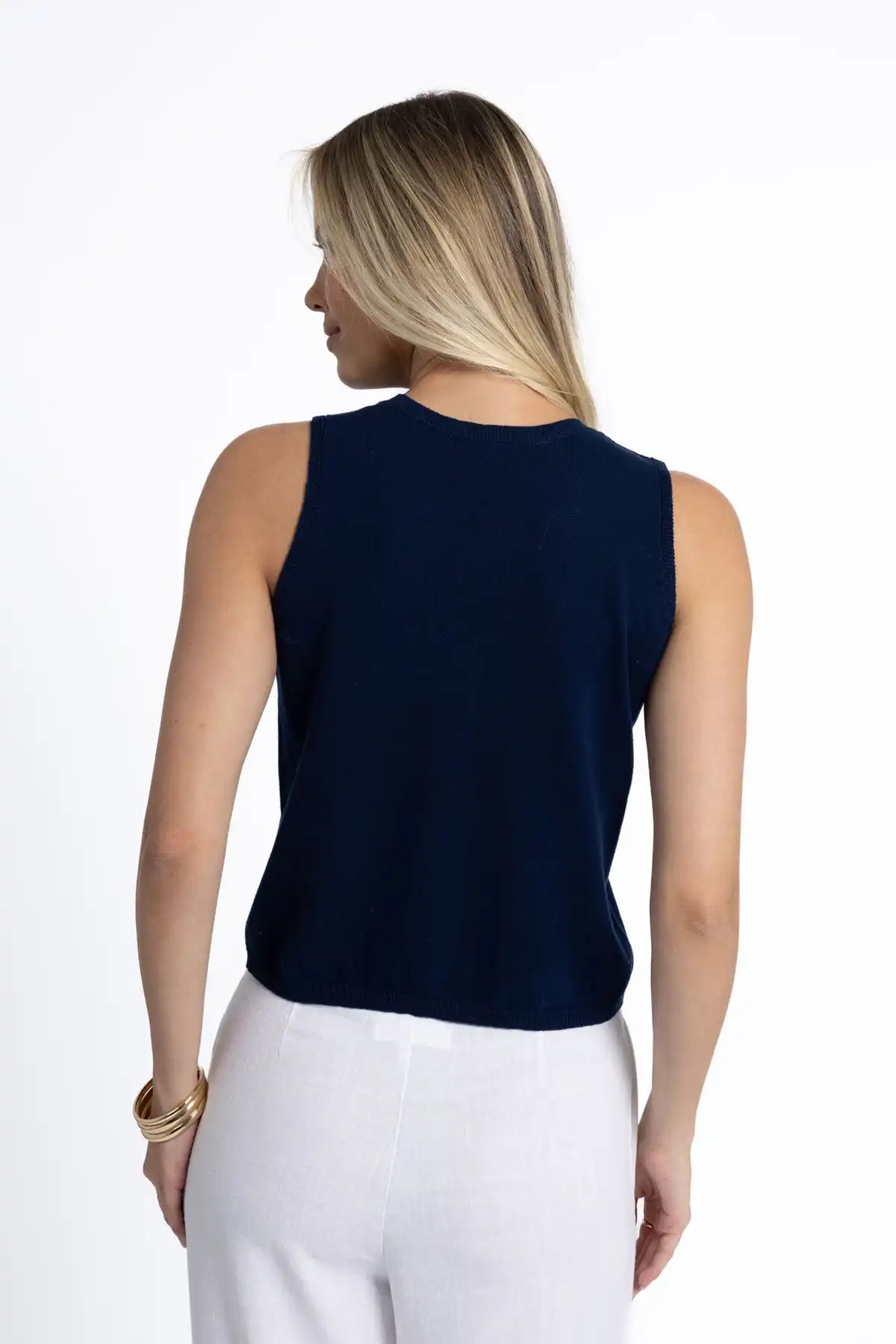 Woman wearing a Humidity Collette Tank in Deep Navy and white pants standing back to camera on a white background