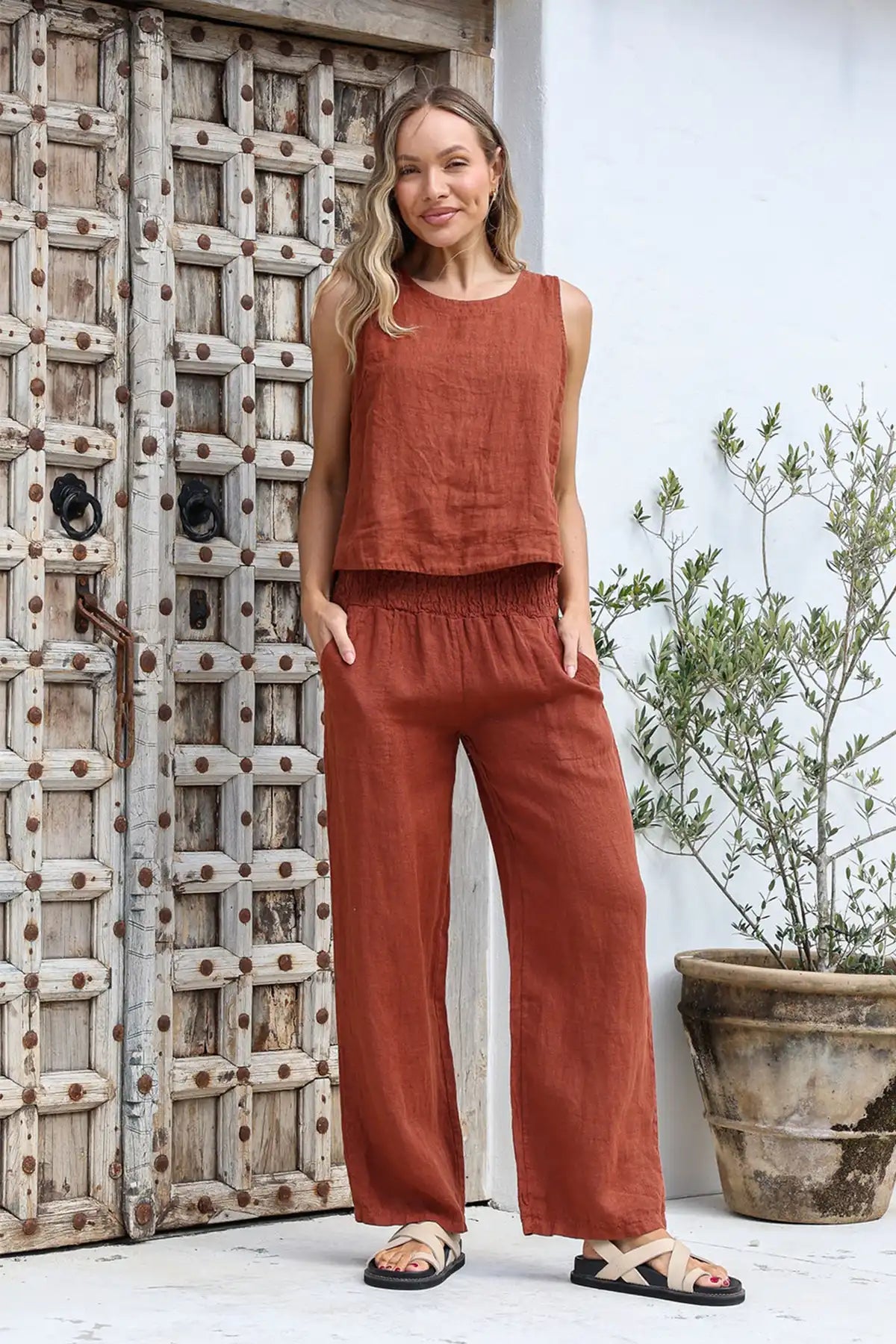 Woman wearing a coc-colored sleeveless top and Isabella Italian Linen Pant in Coco standing in front of a wooden door.