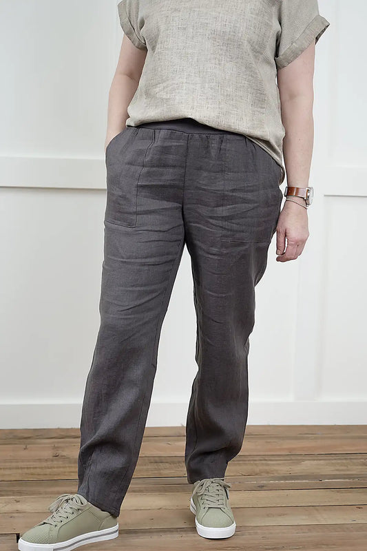 Person wearing Lina Linen Pull-On Pants in Charcoal and a beige shirt standing on a wooden floor with a white wall background