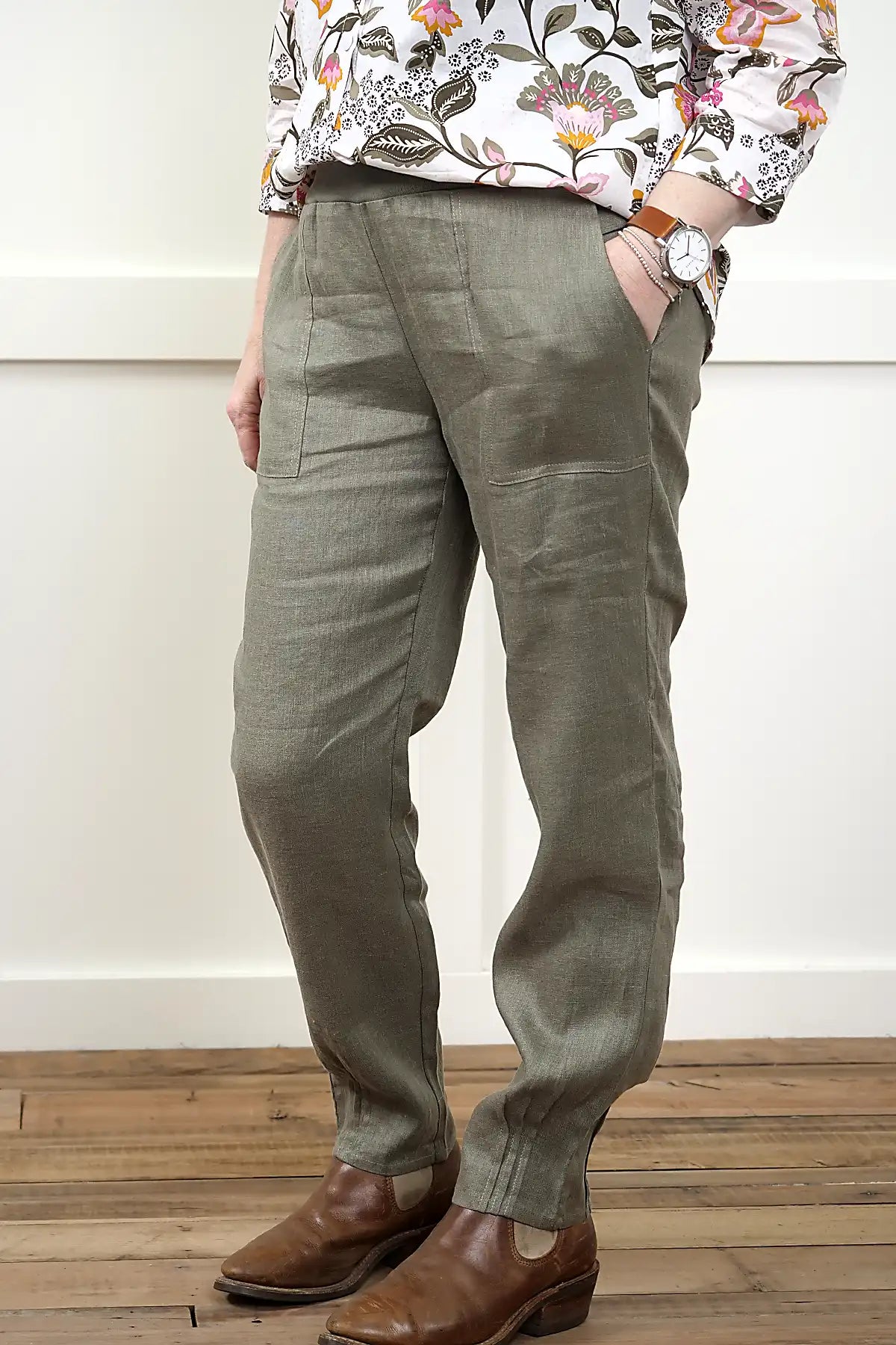 Person wearing Lina Linen Pull-On Pants in Olive viewed from the side and a floral shirt on a wooden floor.