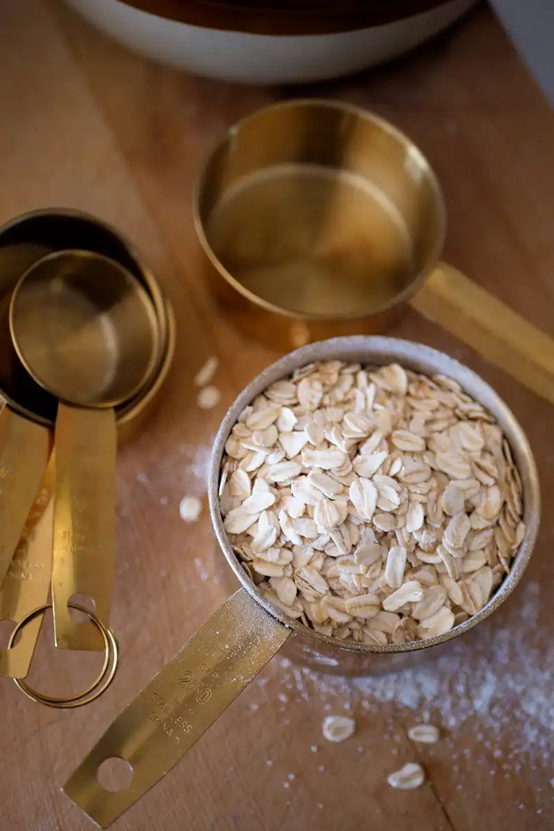 Gold measuring cups filled with oats on a wooden board
