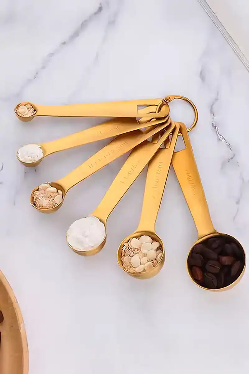 Set of gold measuring spoons with various ingredients on a marble surface