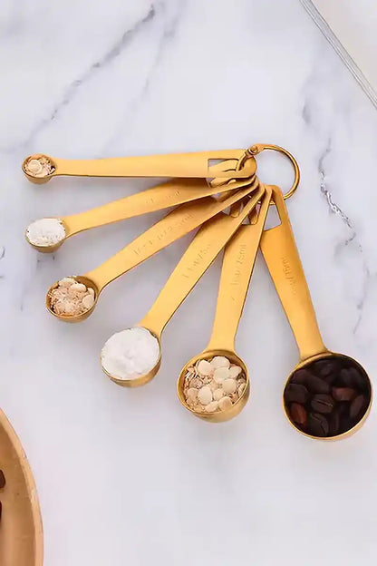 Set of gold measuring spoons with various ingredients on a marble surface