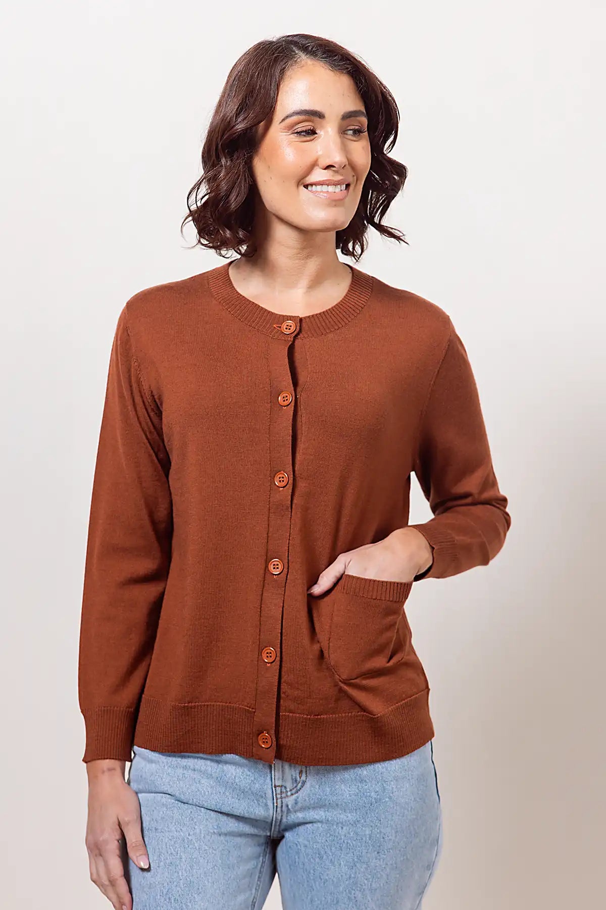Woman wearing a copper merino cardigan and blue jeans against a plain background