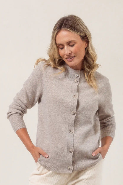Woman wearing a merino wool cardigan in a wheat colour against a plain background