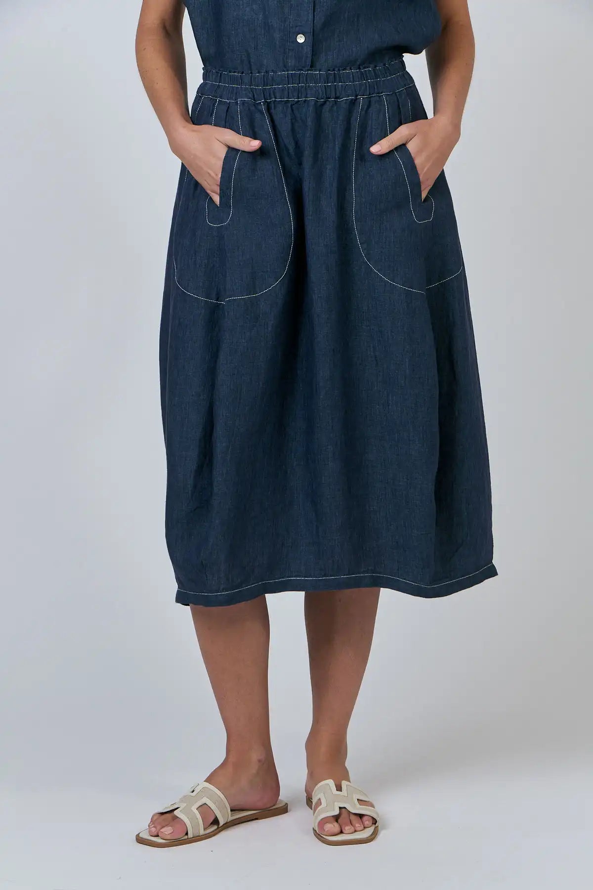 Person wearing a Bay Blue Linen Skirt with a plain background front detailed view with hands in front pockets