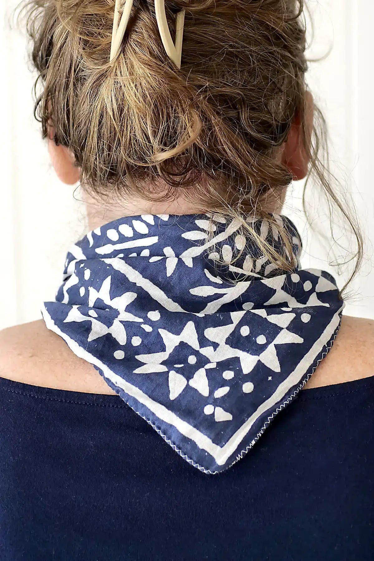 Person wearing a blue and white patterned bandana around their neck against a white background