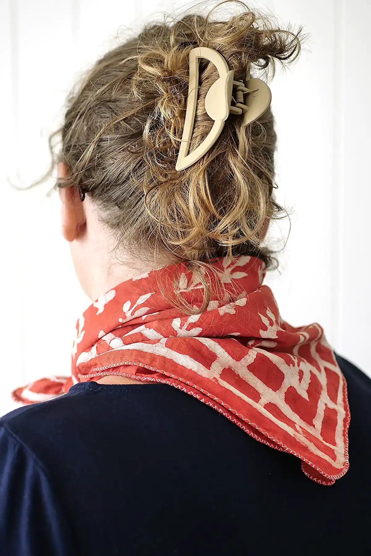 Person wearing a red patterned headscarf and a decorative hair clip against a white background
