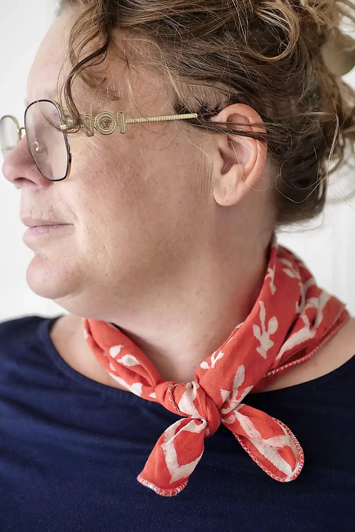 Person wearing a red patterned scarf and glasses with a neutral background