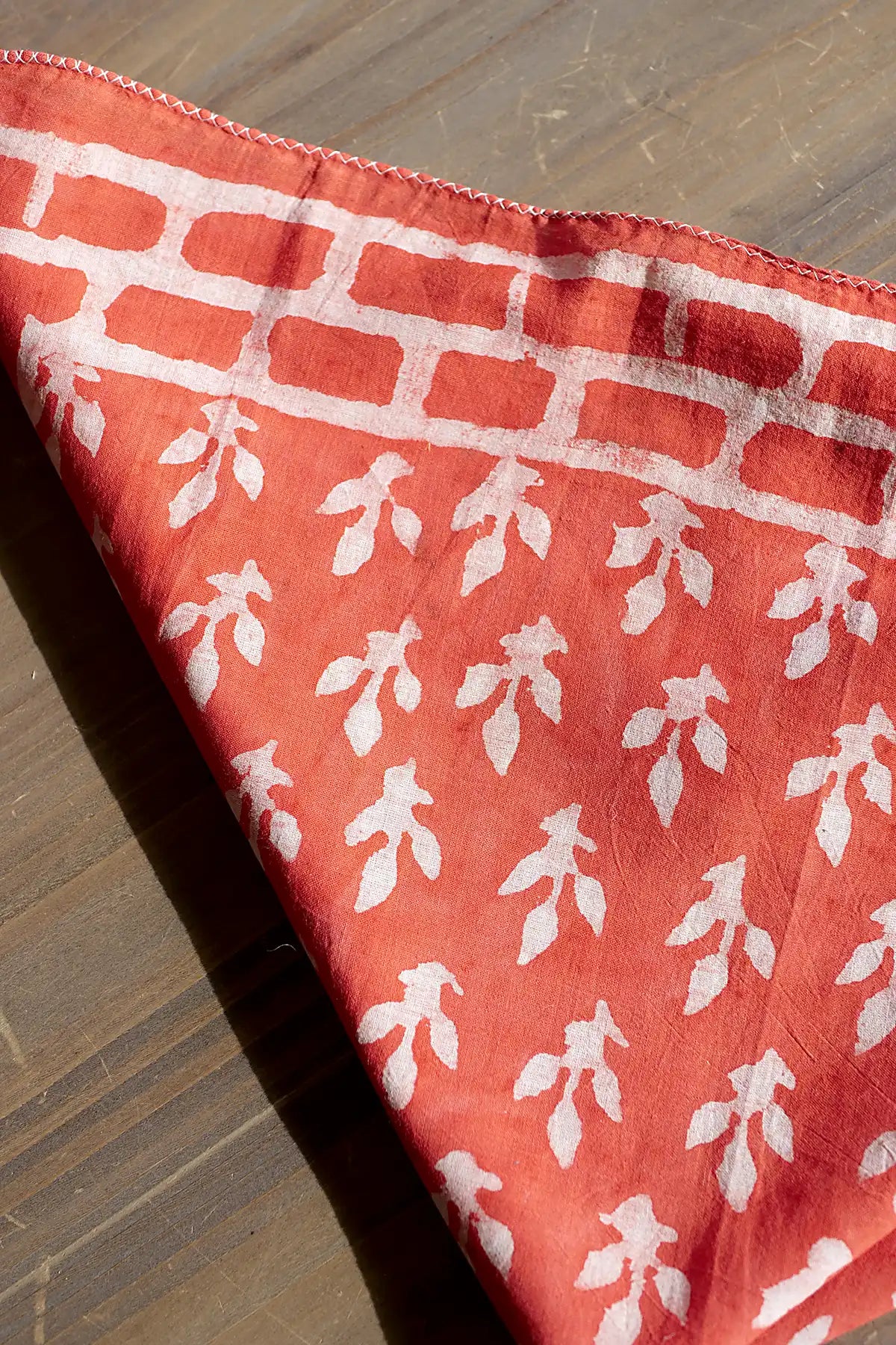 Coral fabric neckerchief with white leaf pattern on a wooden surface