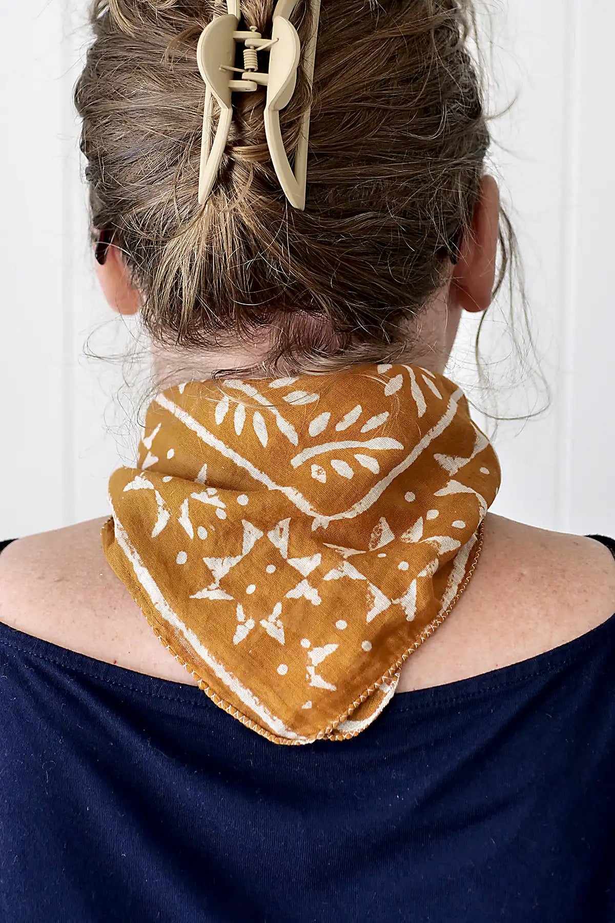 Person wearing a mustard yellow patterned scarf over a navy blue top with a white background
