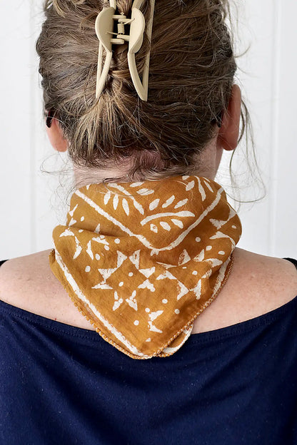 Person wearing a mustard yellow patterned scarf over a navy blue top with a white background