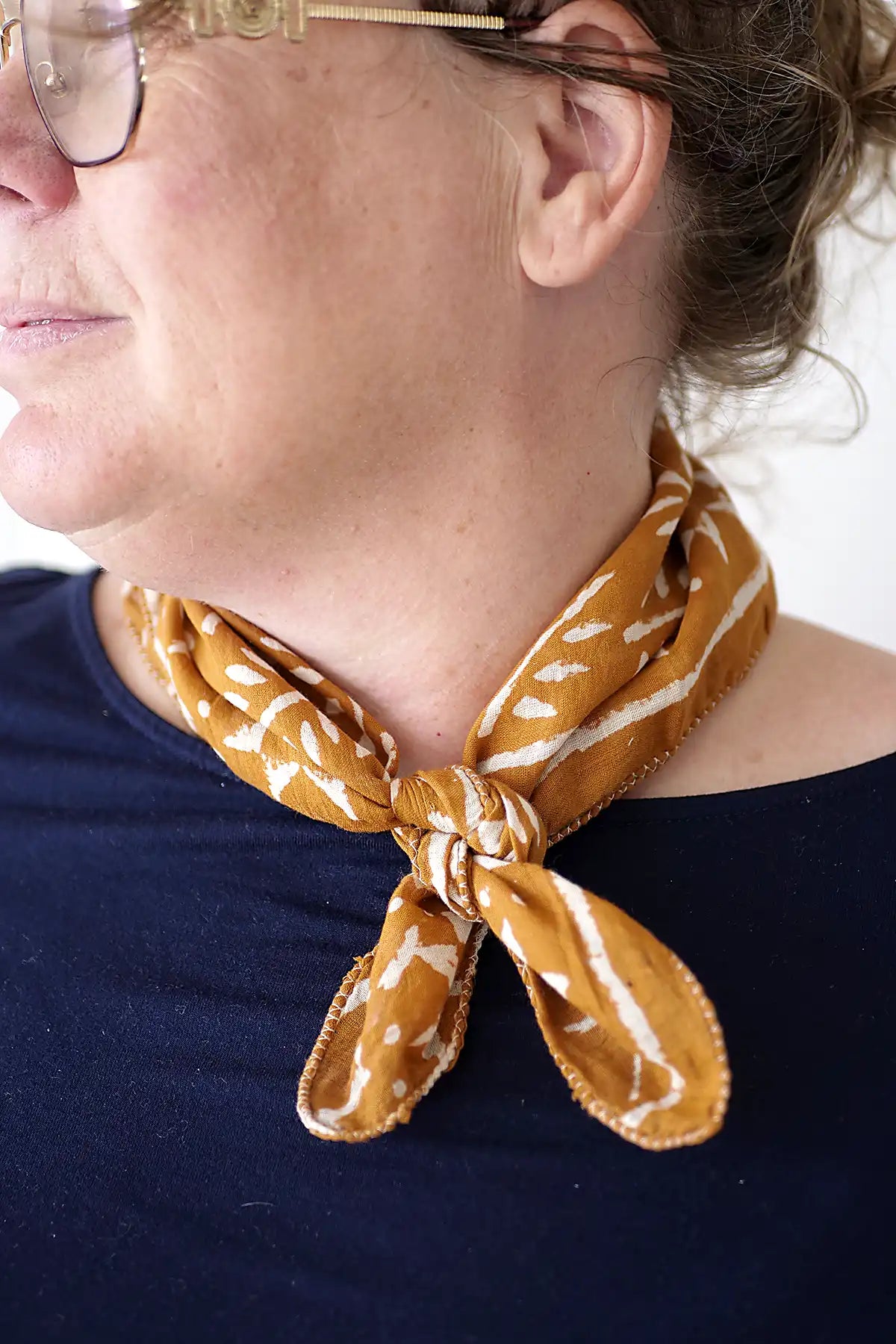 Person wearing a mustard yellow patterned scarf around their neck against a white background