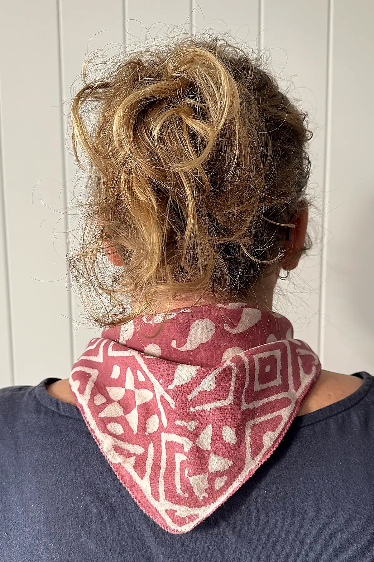 Person wearing a red and white patterned scarf with a neutral background back view