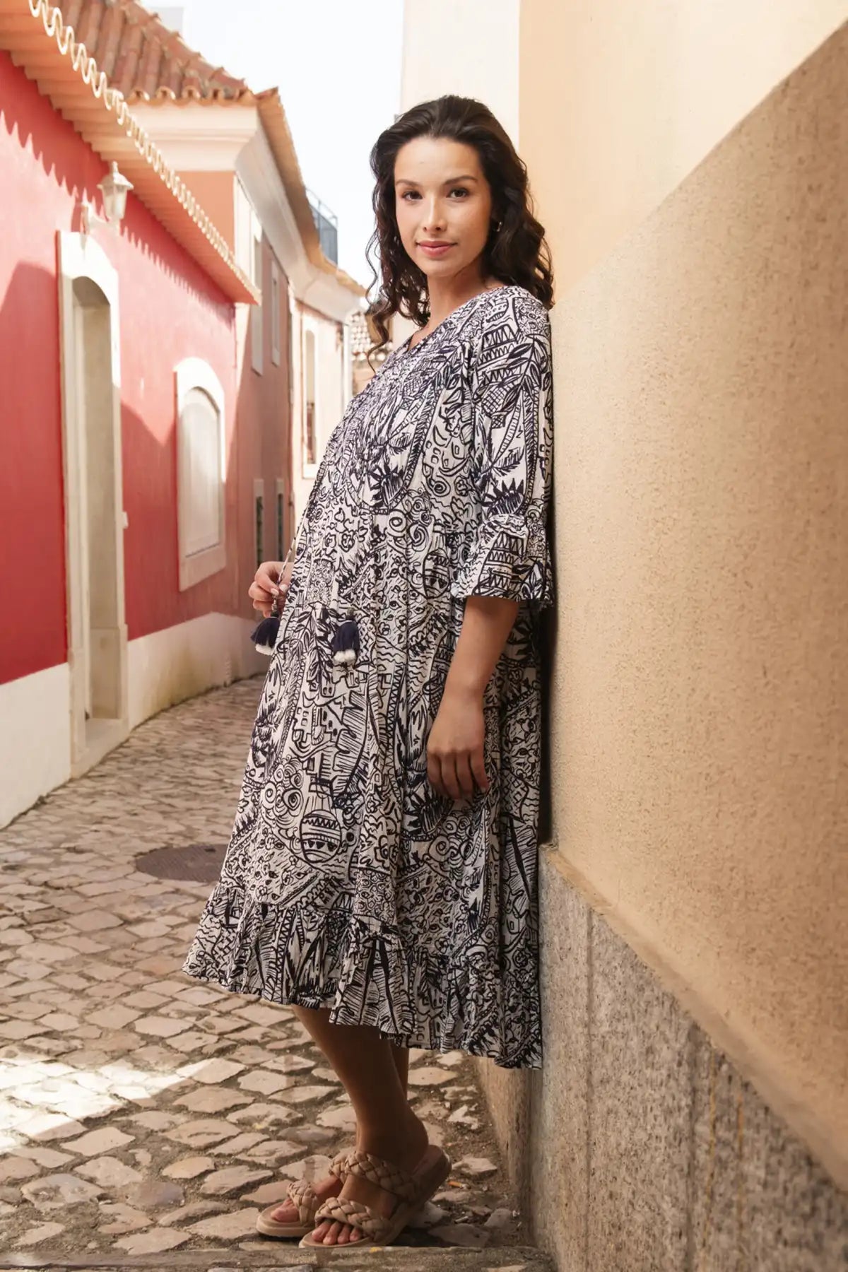 Woman in a  Orientique Aksharay Navy Dress standing against a wall in a sunlit street.