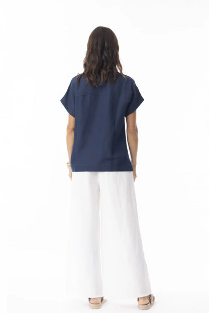 Person wearing a Orientique Escape Linen Solid Boxy Navy Top and white pants on a white background back view