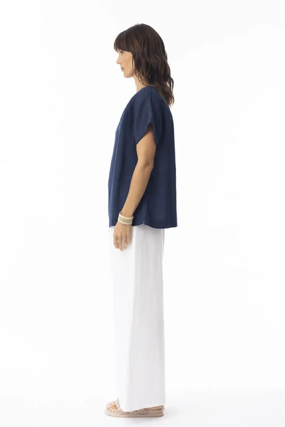 Woman wearing a Orientique Escape Linen Solid Boxy Navy Top and white pants on a white background