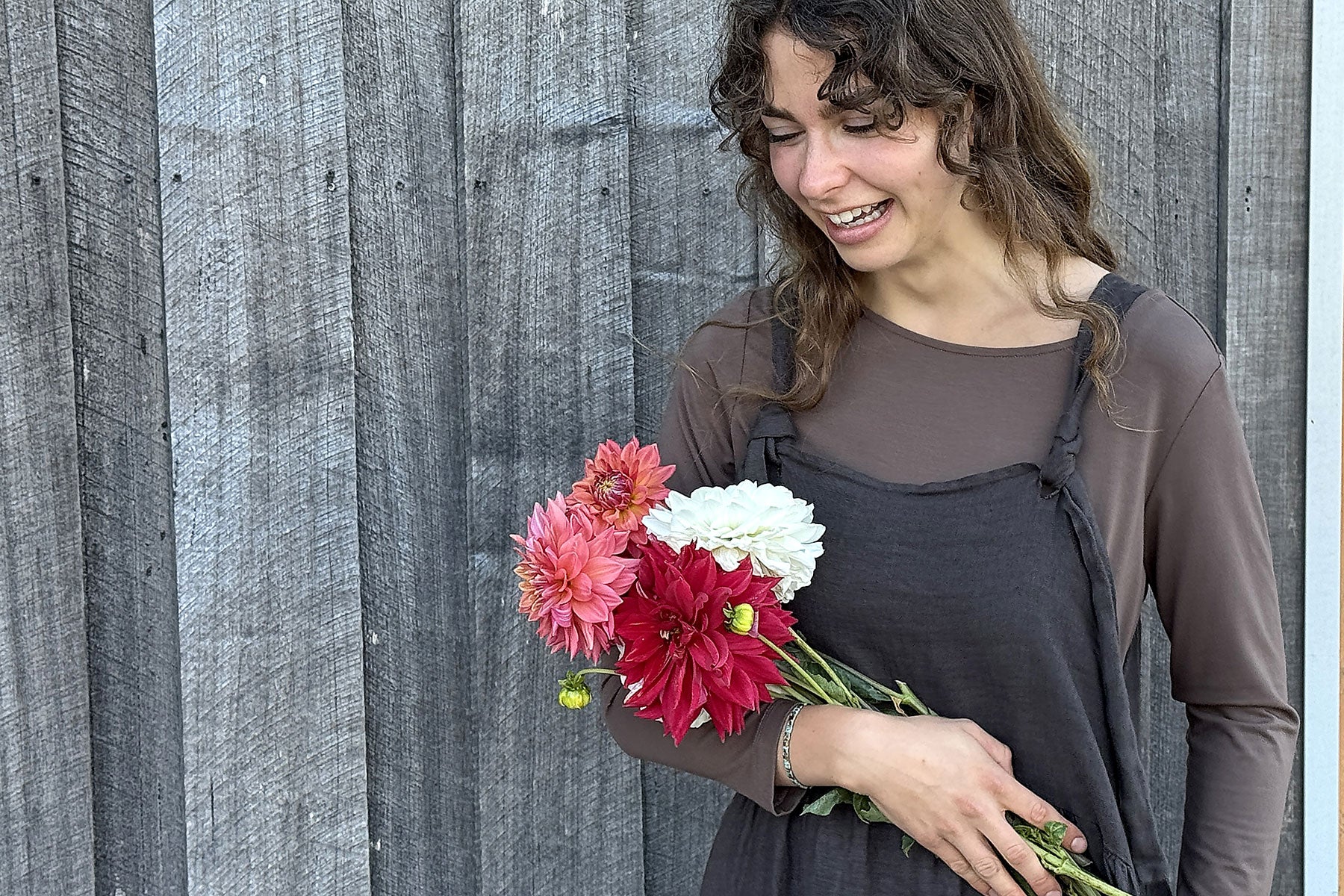 Woman holding a bouquet of flowers against a wooden fence