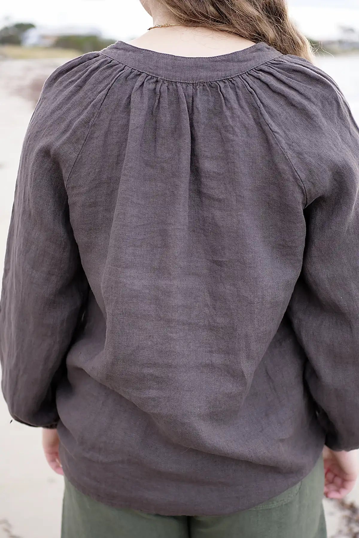 Person wearing a chocolate top with puffed sleeves on a blurred outdoor background