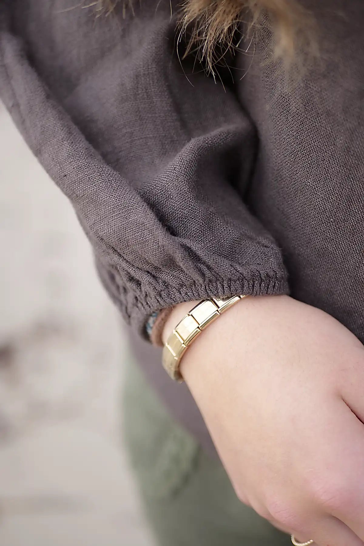 Close-up of a person wearing choloate top with detiled view of sleeve cuff and a gold bracelet on a blurred background