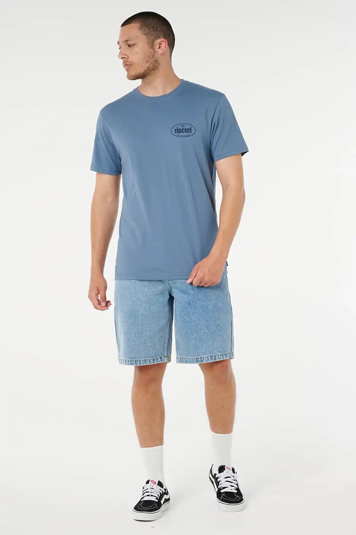 Man wearing a blue t-shirt with Rip Curl Logo and denim shorts on a white background