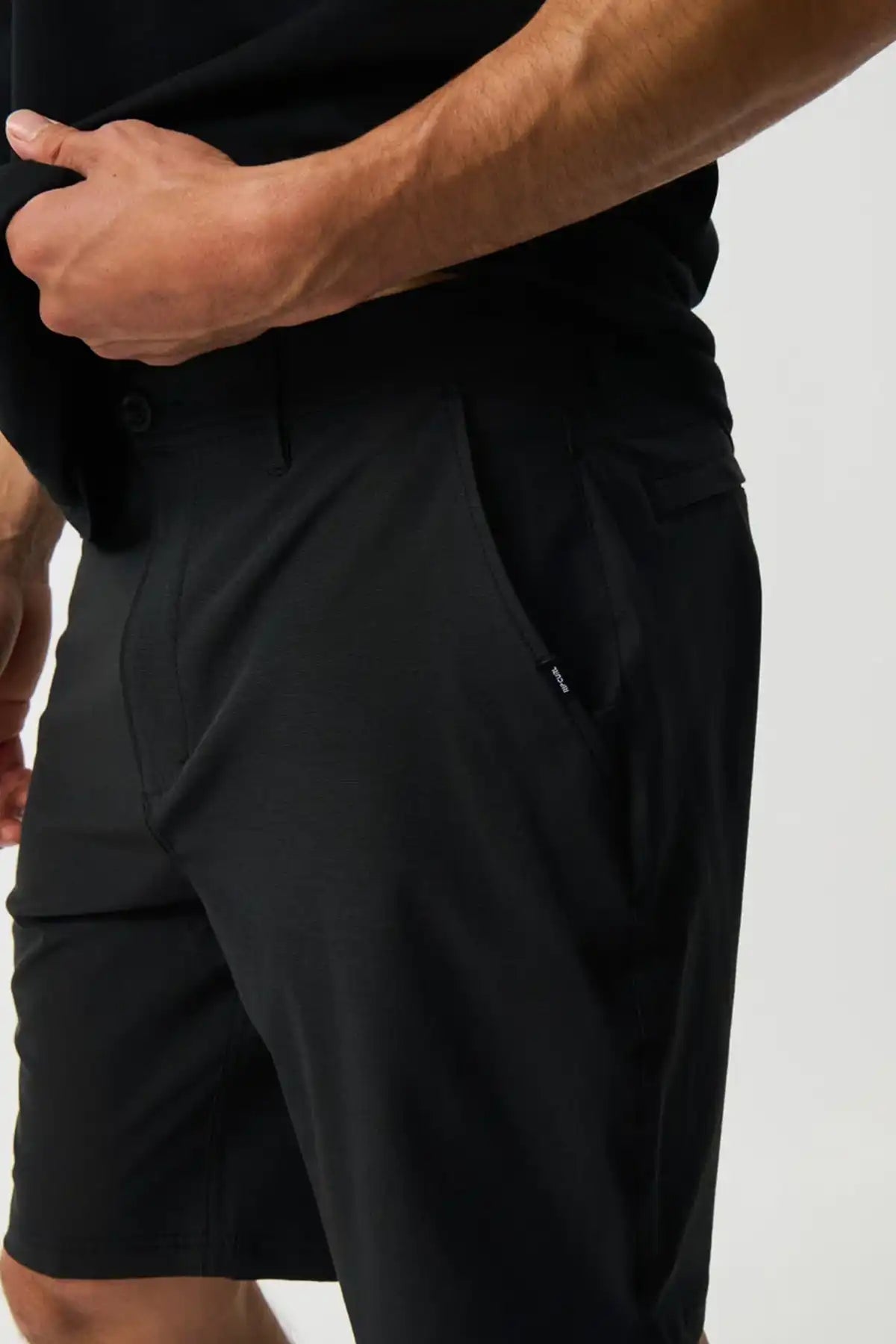 Person wearing black shorts on a plain background front pocket detail view