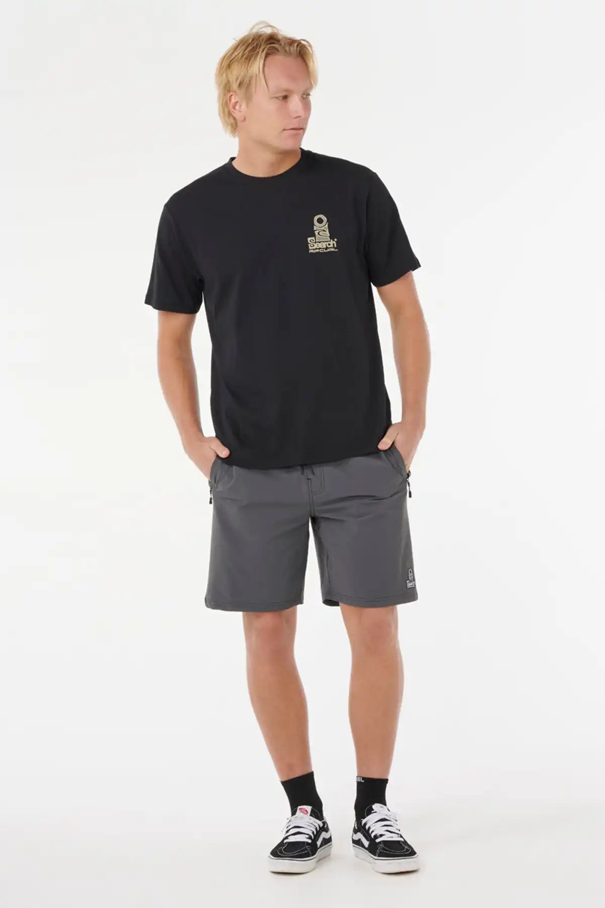 Man wearing a Rip Curl Mens Vaporcool Search Stack Tee -in Black/Olive with a logo and gray shorts on a white background