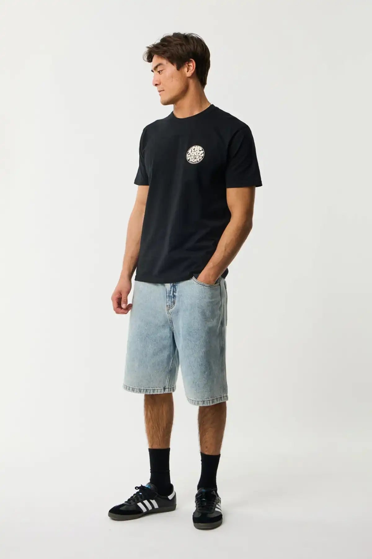Person wearing a black t-shirt with a Rip Curl Wettie logo and light blue shorts on a white background