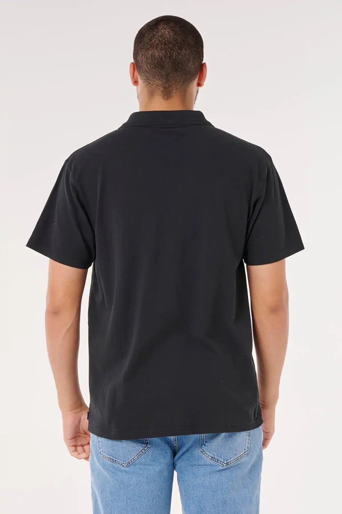 Man wearing a black polo shirt and blue jeans on a white background