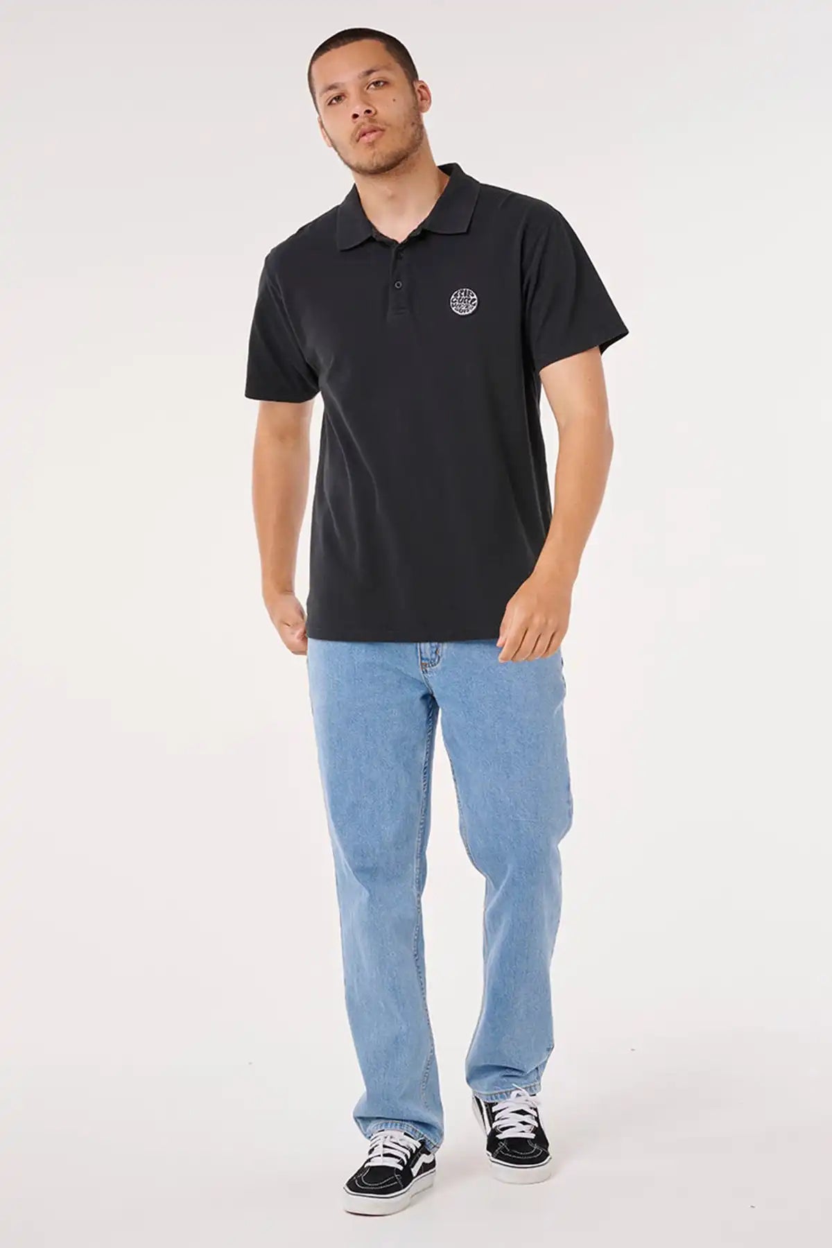Man wearing a black polo shirt with a Rip Curl logo and light blue jeans on a white background