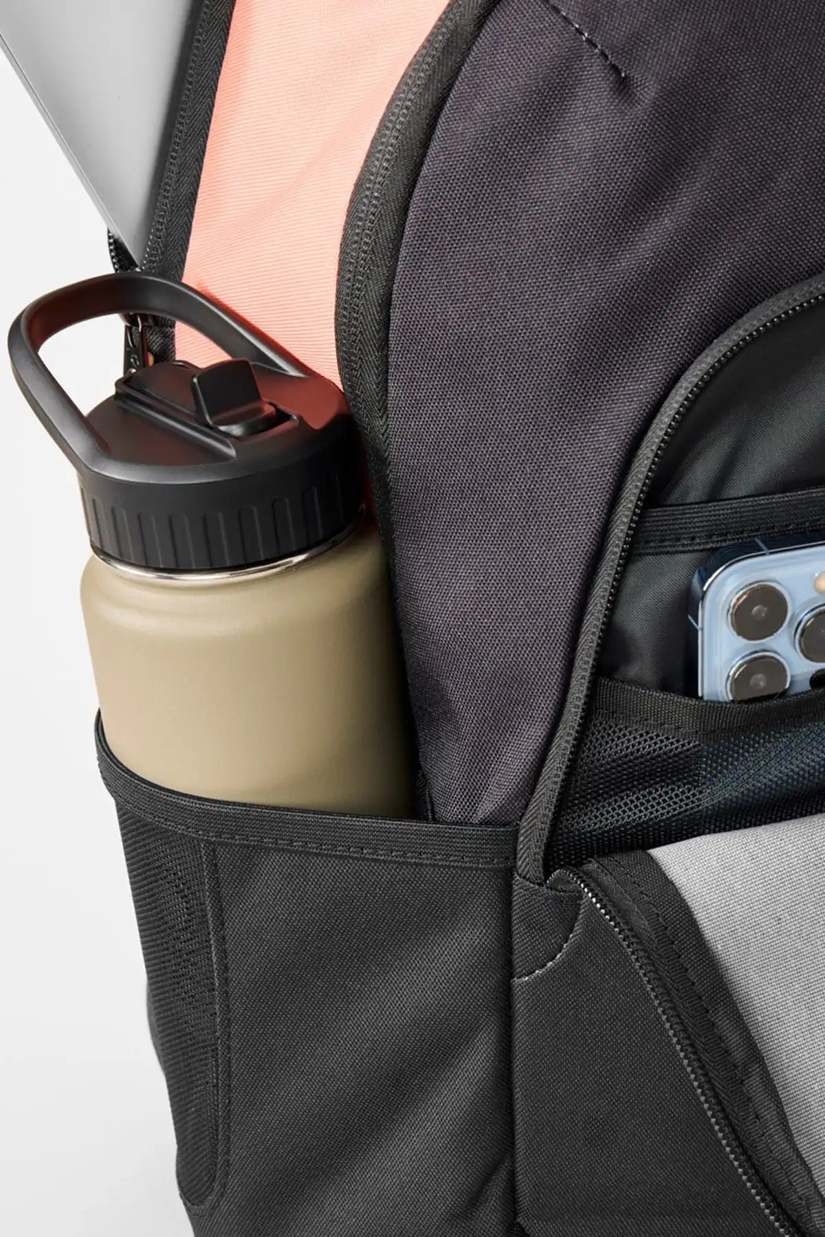 Close-up of a backpack with a water bottle and phone in a pocket on a white background