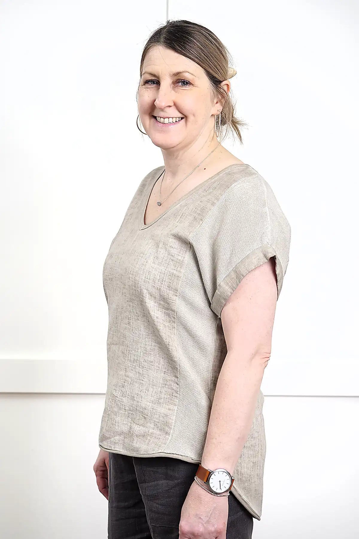 Woman wearing a Rosa V Neck Linen Top in Latte 3/4 side view and dark pants against a white background