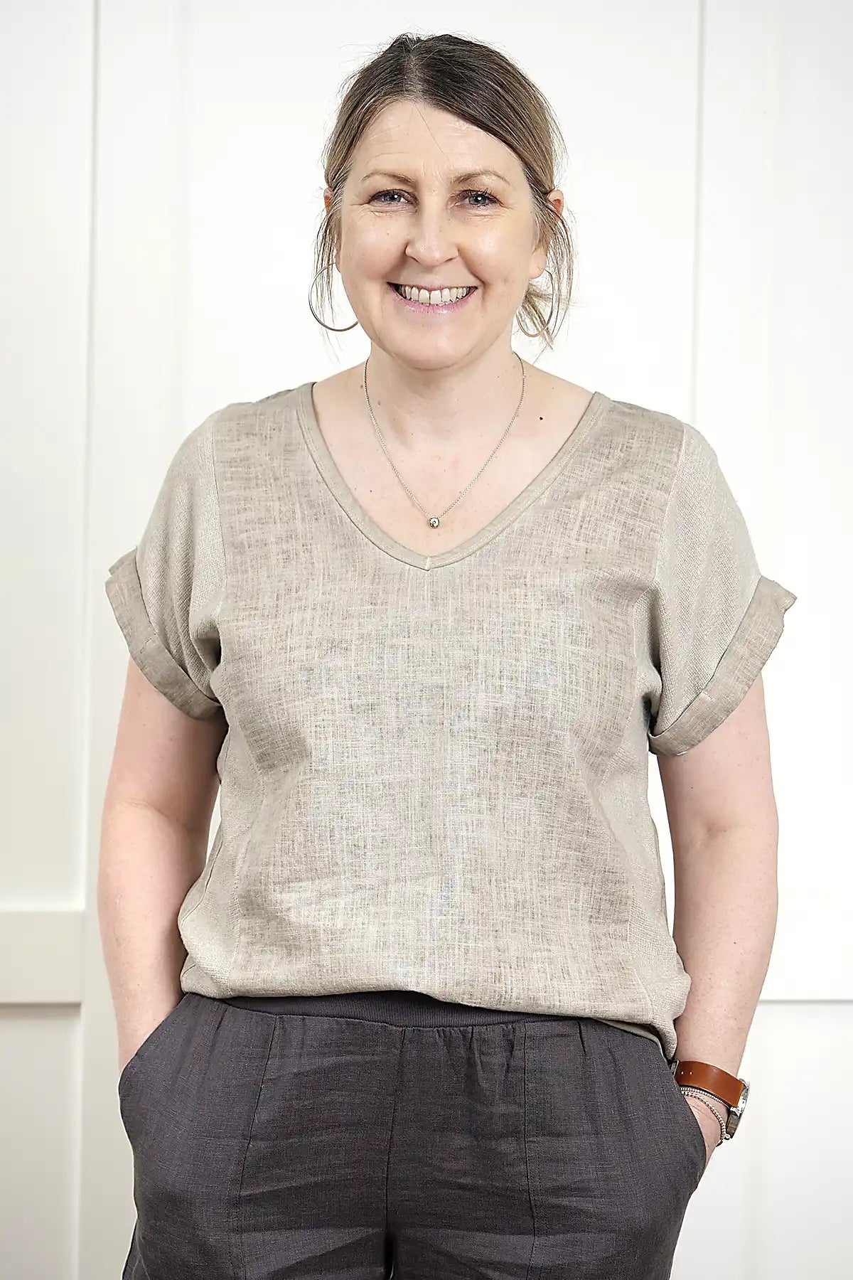 Woman wearing a Rosa V Neck Linen Top in Latte and dark pants against a white background