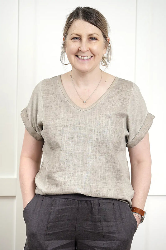Woman wearing a Rosa V Neck Linen Top in Latte and dark pants against a white background