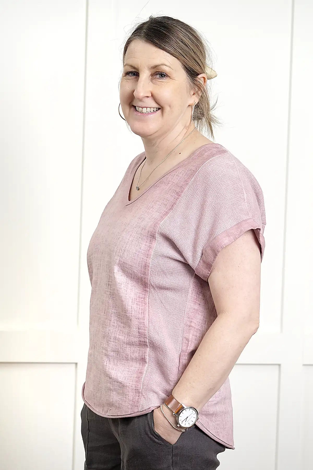 Woman wearing a Rosa V Neck Linen Top in Pink and dark pants against a white background