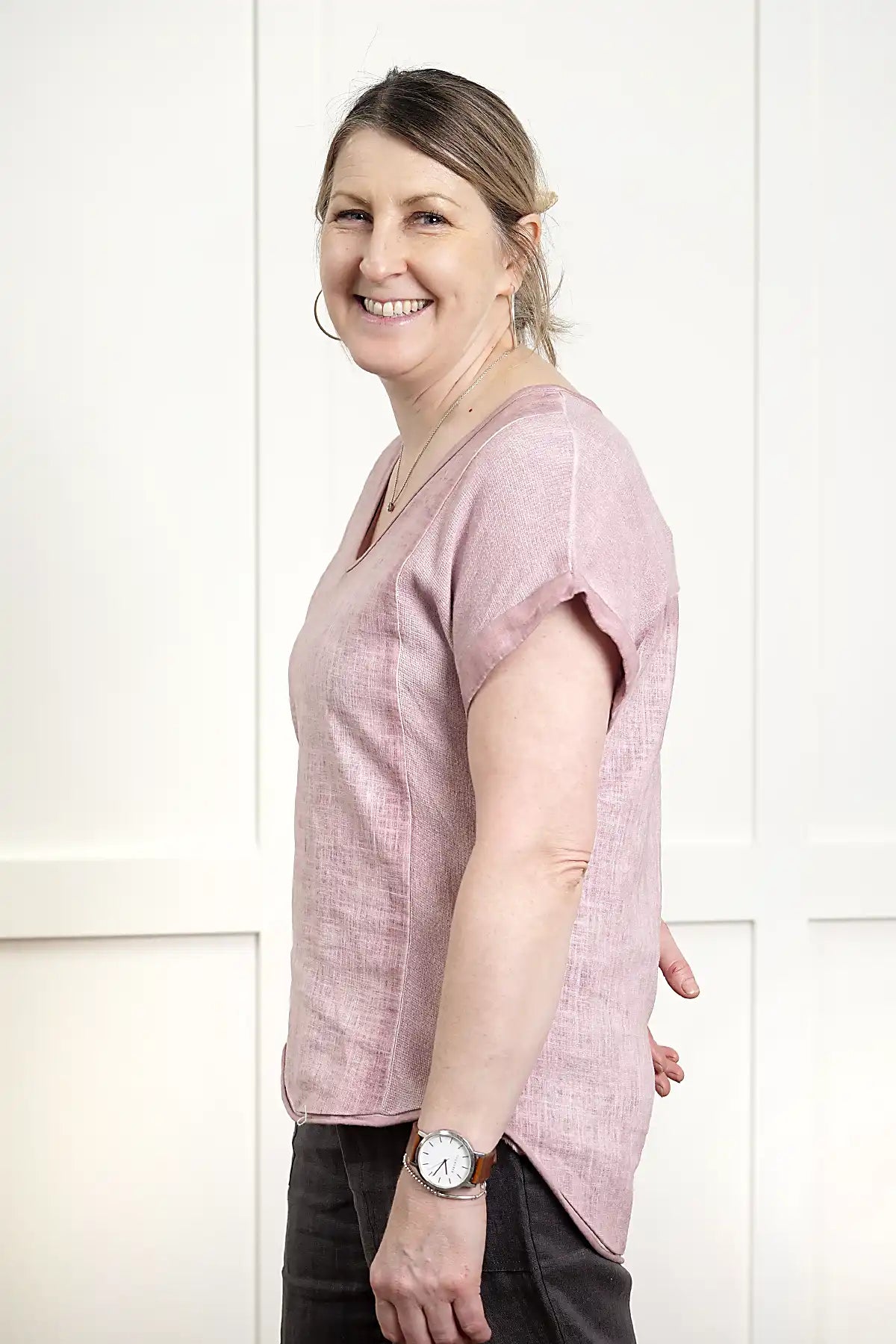 Woman wearing a Rosa V Neck Linen Top in Pink standing side on against a white wall