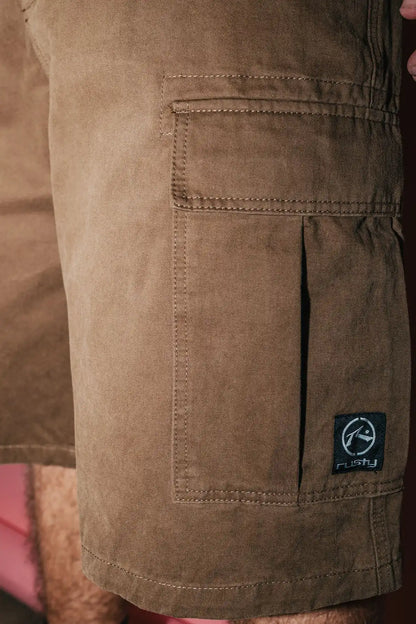 Close-up of Rusty Commando 23" Baggy Cargo Short in Pinecone with a brand logo on the pocket.