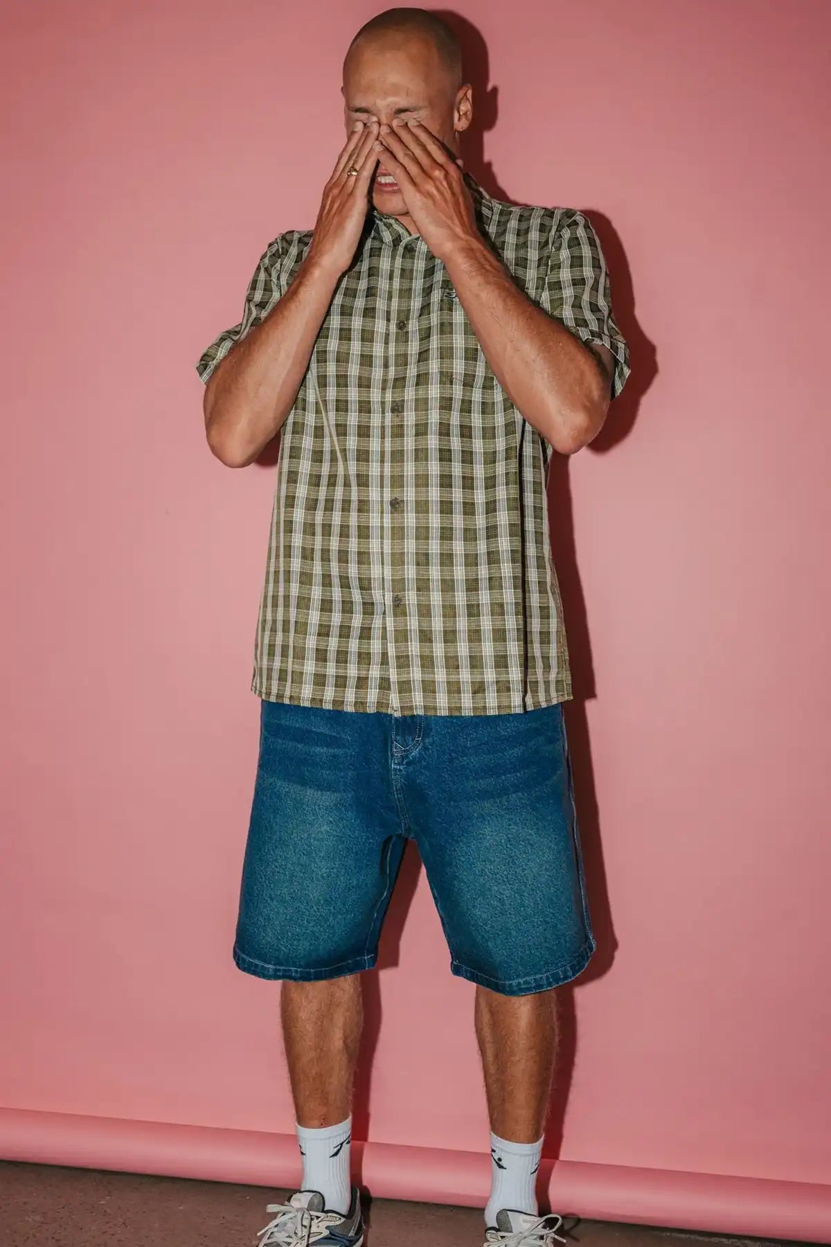 Man wearing a plaid shirt and shorts against a pink wall