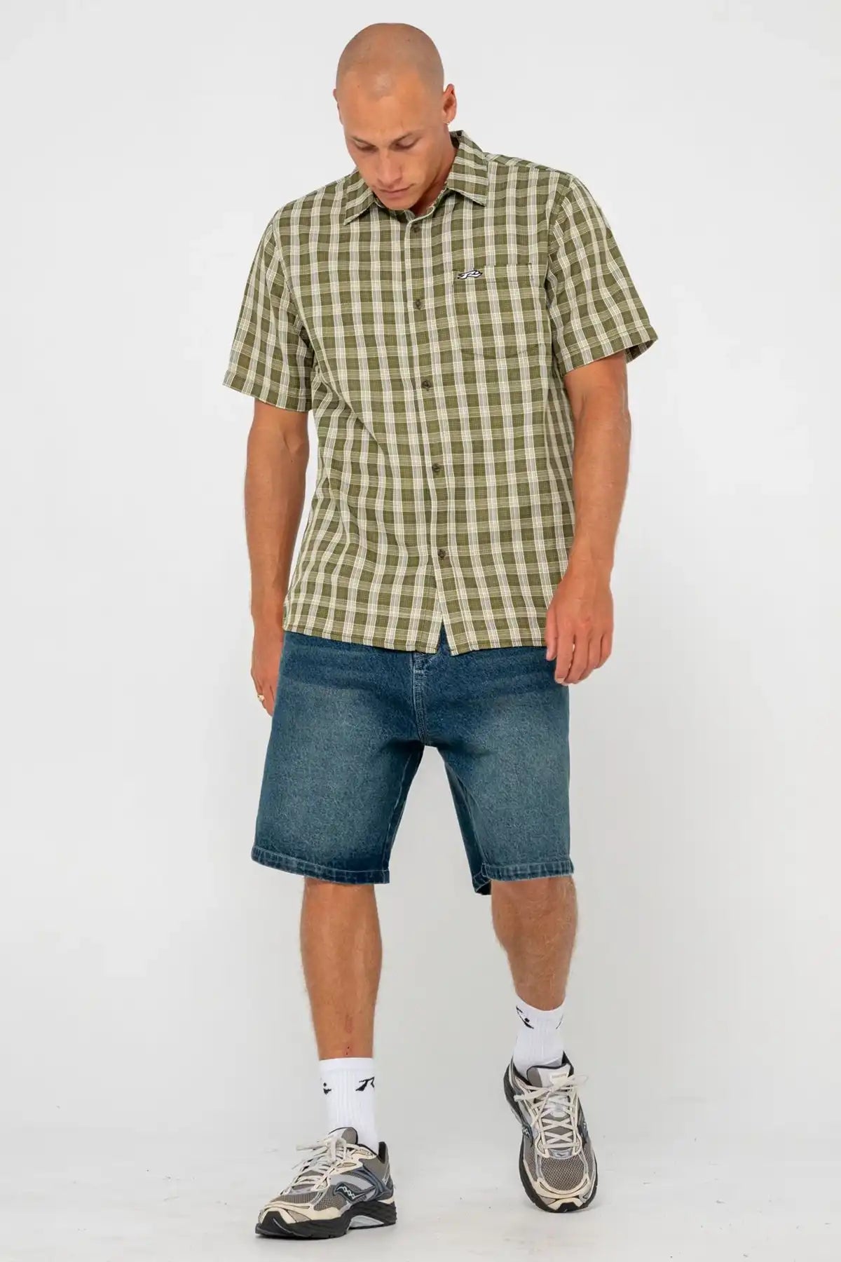 Man wearing a green checkered Rusty shirt and blue shorts on a white background